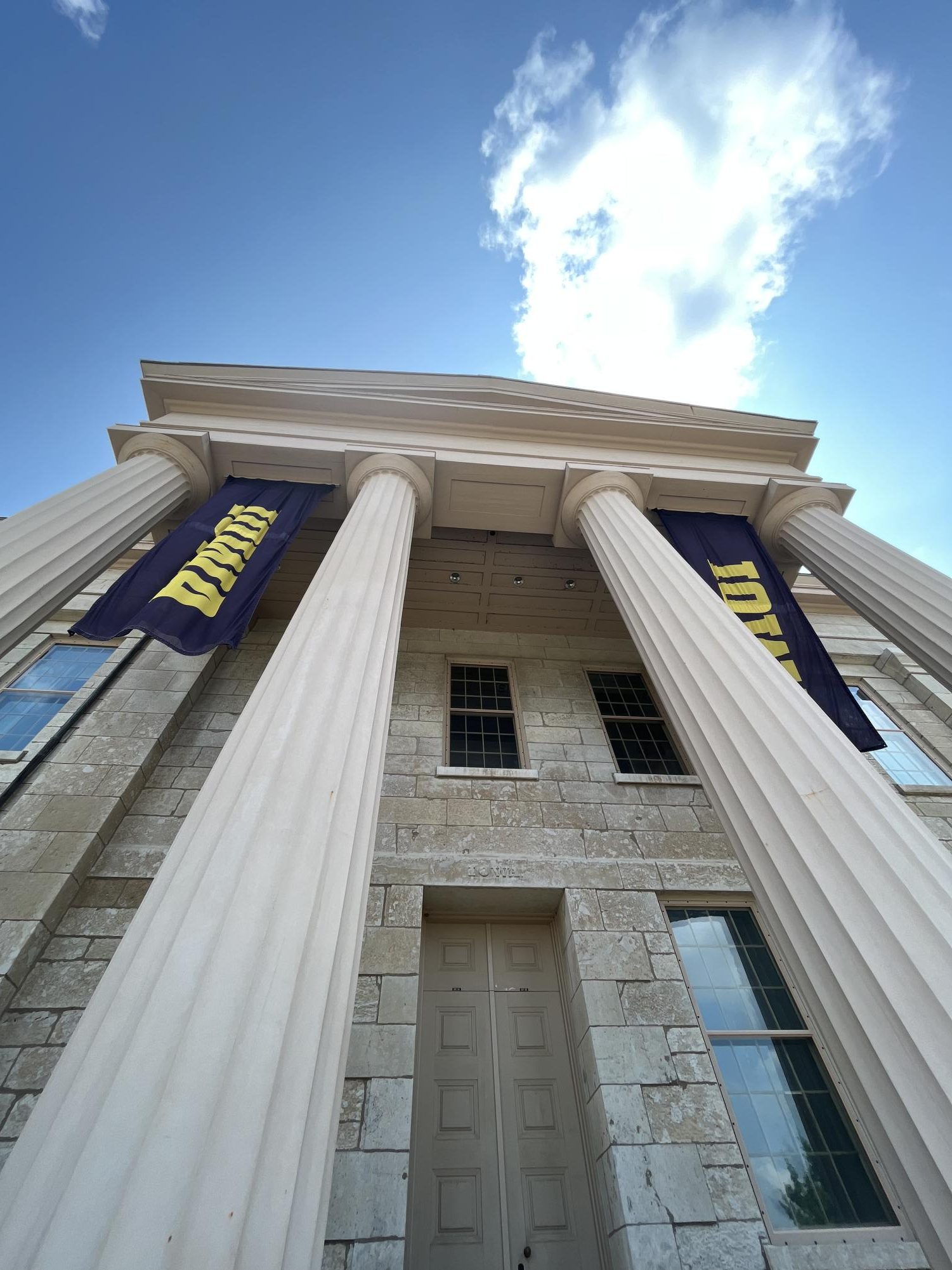 On the Old Capitol, located within the University of Iowas campus, banners with the college logo are hung from the pillars on the front of the building.
