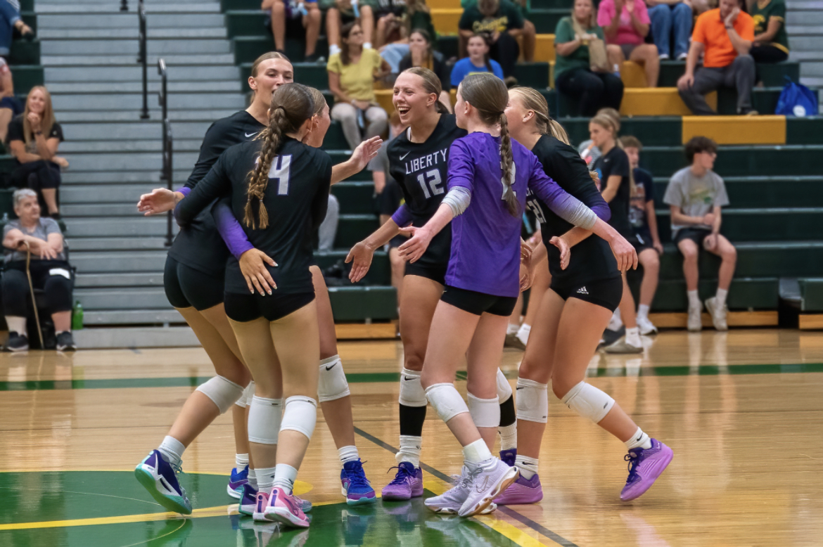 The Liberty volleyball team huddles together, celebrating  after making a significant play. 